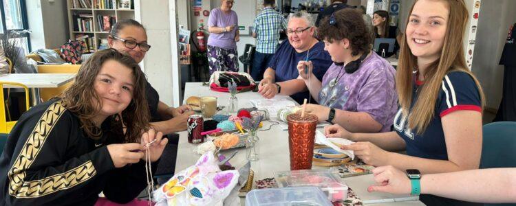 A group of three young people and two parents in the hidden gem cafe creating textile art on a white table