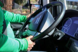 a photo of a person wearing a green sweater in the drivers seat of a van holding a steering wheel